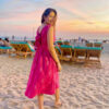 Dr.Elakshi Gupta More wearing a Strawberry Pink handloom Ikat midi dress with two pockets, standing on a sandy beach during sunset; sustainable cotton fashion by Abravi.