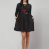 Indian model's front view of artisan - made black Ikat mini dress in breathable cotton with playful red tassel accents.