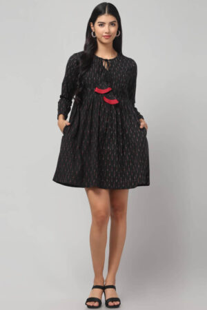 Indian model's front view of artisan - made black Ikat mini dress in breathable cotton with playful red tassel accents.