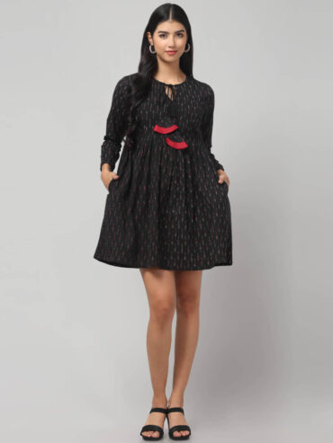 Indian model's front view of artisan - made black Ikat mini dress in breathable cotton with playful red tassel accents.